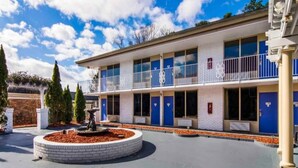 A two-story motel with a central courtyard, a fountain, and a parking area. - Comfy Full Beds|Free Wifi &Parking (LaGrange)