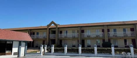 A hotel with a central courtyard, multiple balconies, and a red-roofed building to the left.