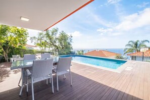 Un espace aménagé au bord de la piscine, avec une table et des chaises, entouré d’une terrasse en bois et d’une clôture en métal.