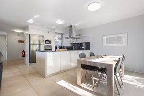 A modern kitchen with white cabinetry, a central island, and a dining area with a wooden table and chairs. - Vila Bela by Your Madeira Rentals (Arco da Calheta)
