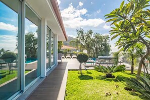 A modern house with large glass windows, a wooden deck, a swimming pool, and a well-maintained garden. - Vila Bela by Your Madeira Rentals (Arco da Calheta)