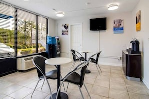Hotellihuone, jossa on ruokailutila, vesiautomaatti, taulutelevisio ja ikkuna, jossa on sälekaihtimet.