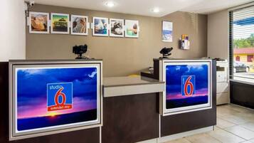 En hotelreception med to skærme, der viser '6' logoet og teksten 'extended stay', et kamera til venstre og billeder i rammer på væggen.