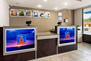 A hotel reception desk with two monitors displaying the '6' logo and 'extended stay' text, a camera on the left, and framed pictures on the wall. - Comfy  Full Beds|Free Wifi &Parking (LaGrange)