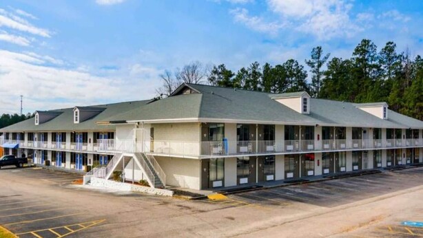A motel with a central building and attached wings, featuring a parking lot and a clear sky. - Comfy Full Beds|Free Wifi &Parking (LaGrange)