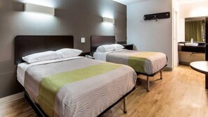A hotel room with two beds, a small bedside table, a wall-mounted light, and a bathroom with a mirror and sink. - Comfy Full Beds|Free Wifi &Parking (LaGrange)