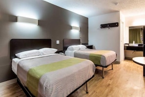 Hotellihuone, jossa on kaksi sänkyä, pieni yöpöytä, seinään kiinnitetty valaisin sekä kylpyhuone, jossa on peili ja pesuallas.