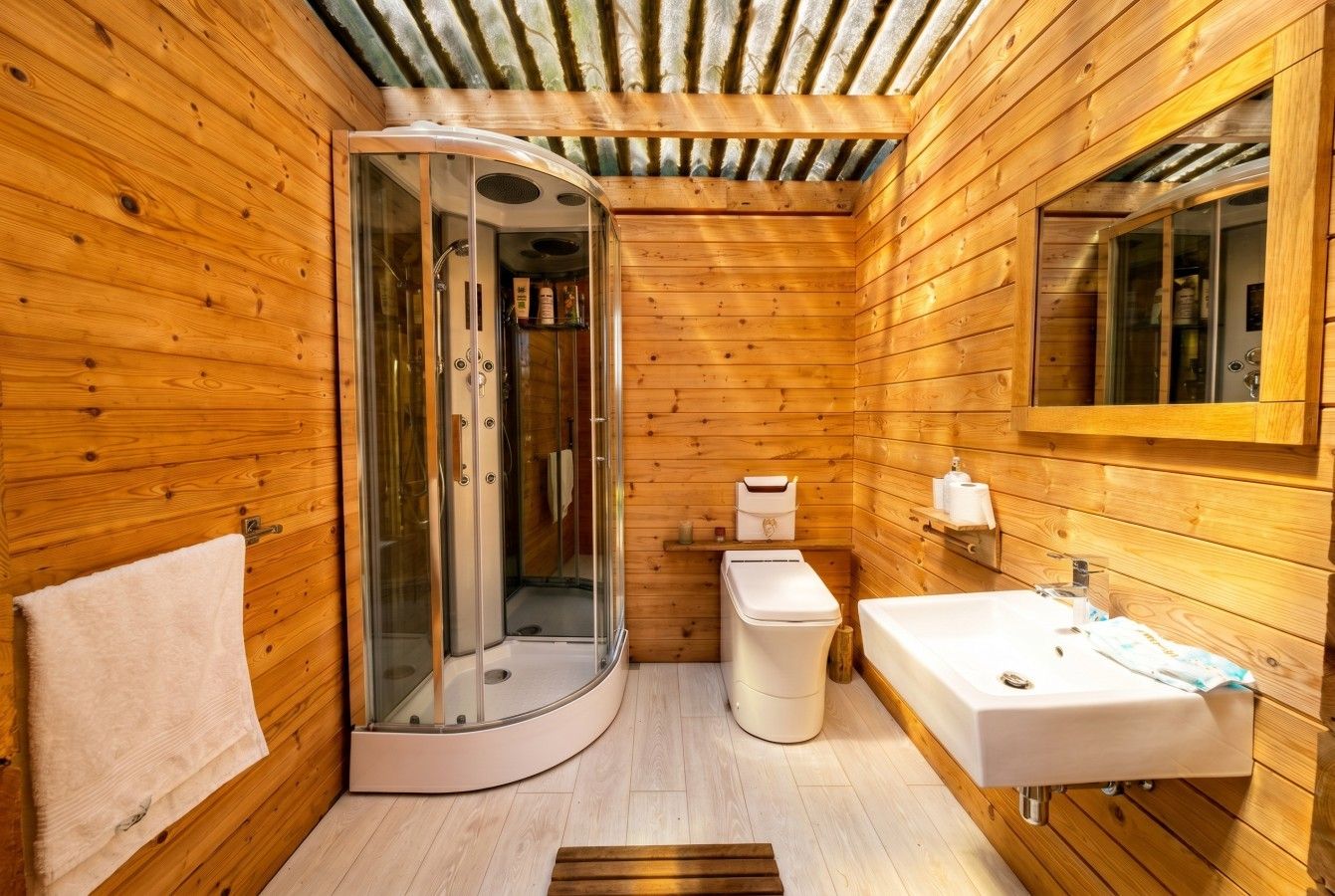 Ein Badezimmer einer Holzhütte mit einer gläsernen Duschkabine, einem weißen Waschbecken und einer Toilette.