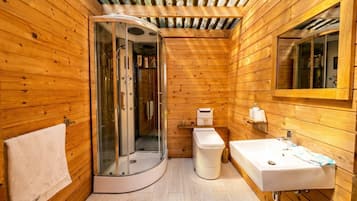 Ein Badezimmer einer Holzhütte mit einer gläsernen Duschkabine, einem weißen Waschbecken und einer Toilette.