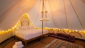 A tent with a bed, a hanging light fixture, and a patterned rug.