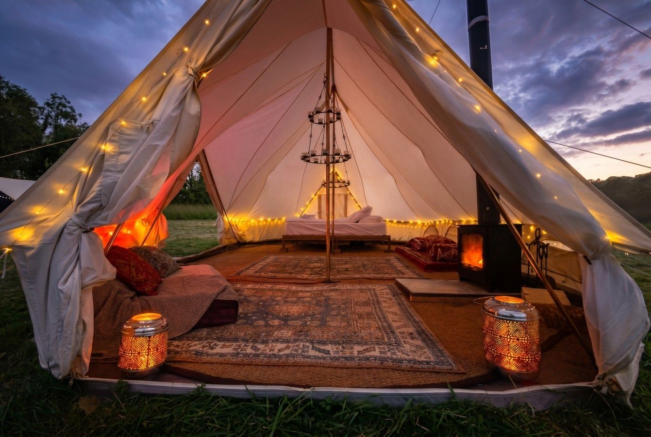 A tent with a bed, a hanging light fixture, and a portable stove.