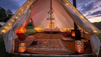 A tent with a bed, a hanging light fixture, and a portable stove.