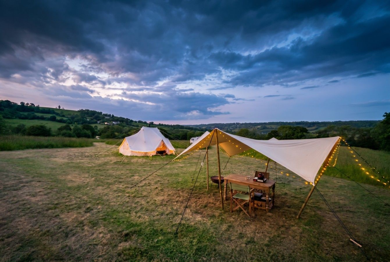Ein Campingplatz mit zwei Zelten und einem Tisch unter einem Blätterdach.