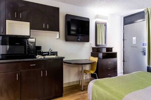 Habitación de hotel compacta con kitchenette, una cama, una mesita y una silla.