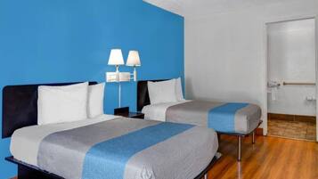 A hotel room with two beds, a nightstand, a lamp, and a door.