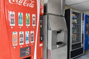 Màquina expenedora amb diverses opcions de begudes, un cendrer i una altra màquina expenedora de llaminatures.