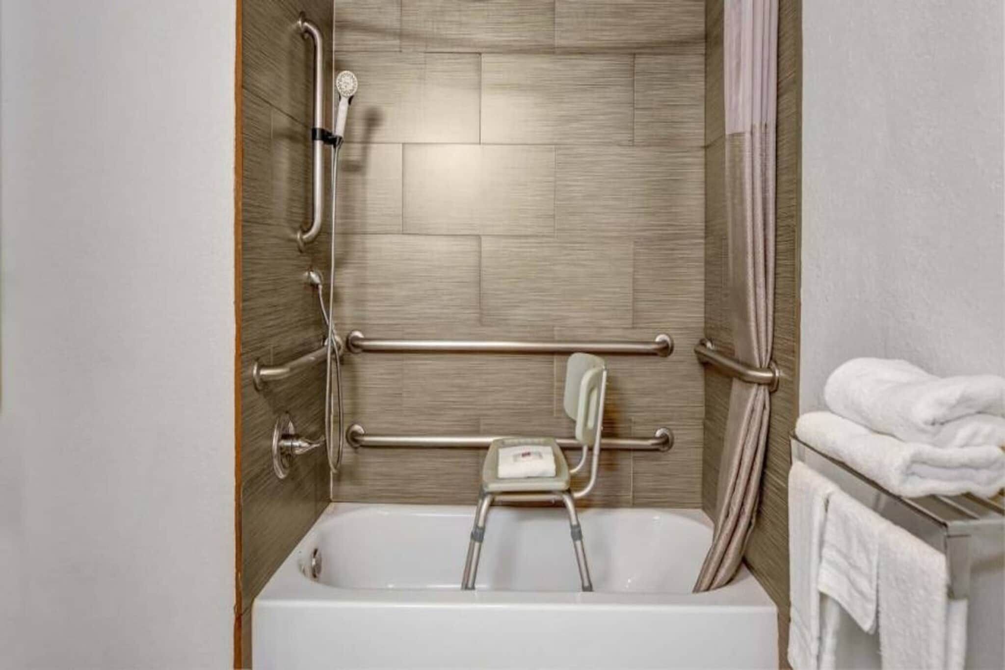 A bathroom with a walk-in shower, grab bars, a small step stool, and a towel rack.