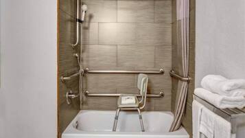 A bathroom with a walk-in shower, grab bars, a small step stool, and a towel rack.