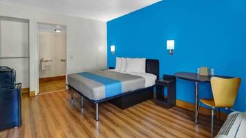 A hotel room with a bed, a desk, a chair, and a suitcase.