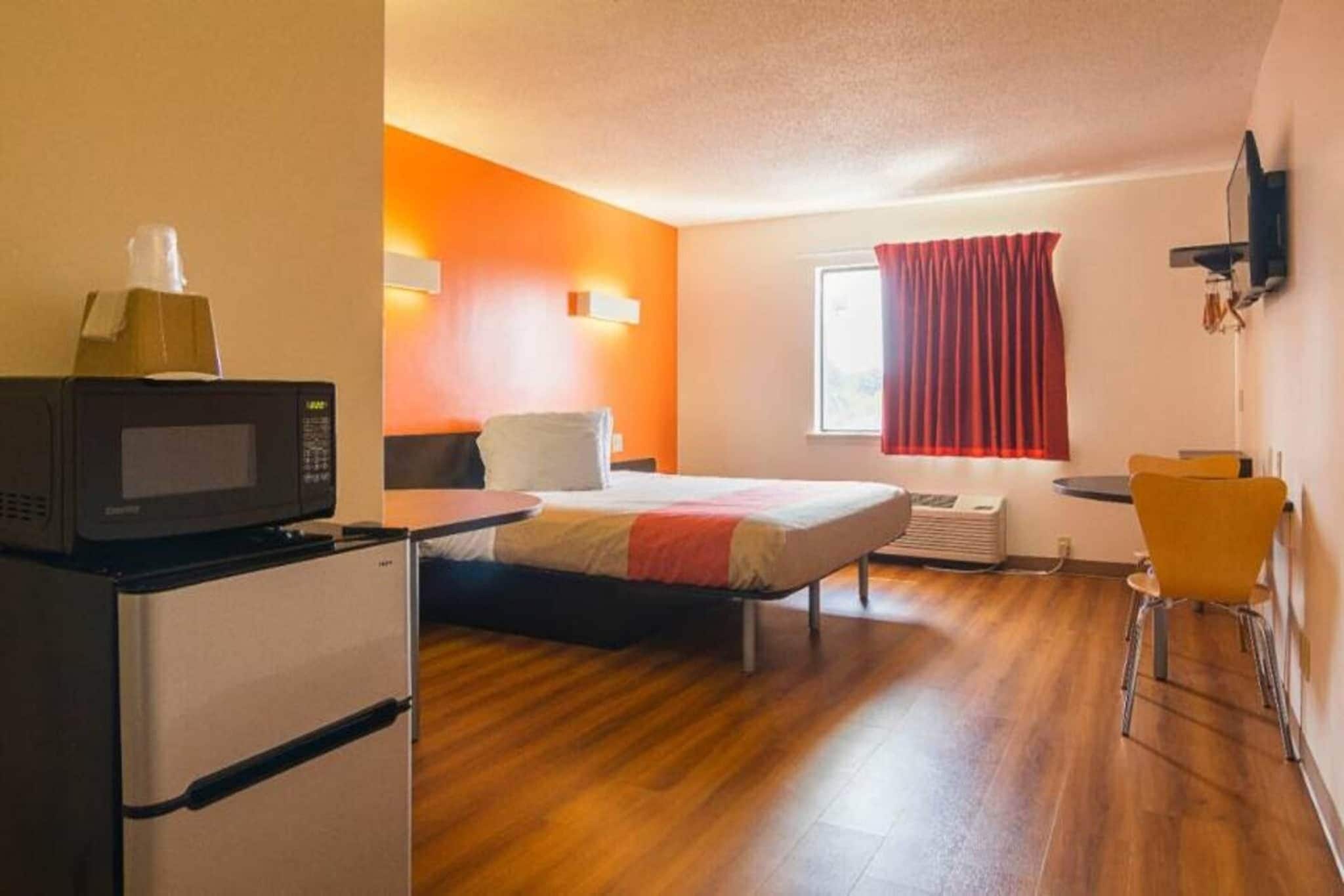 A compact hotel room with a bed, a desk, a microwave, and a chair.