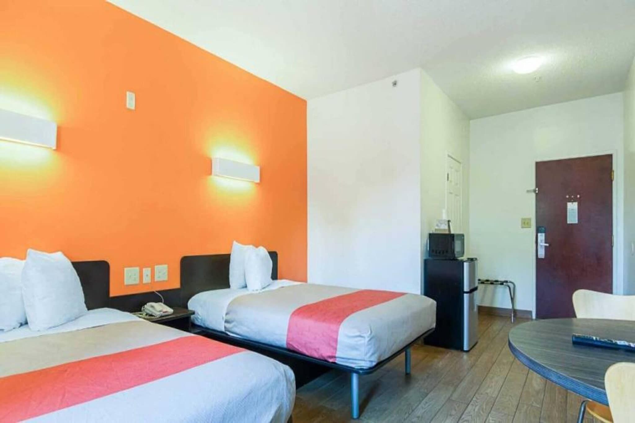 A hotel room with two beds, a desk, a refrigerator, and a door.