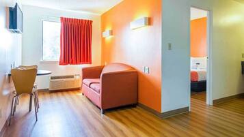 Quarto de hotel com piso de madeira, sofá vermelho, uma mesinha e uma janela com cortinas vermelhas.