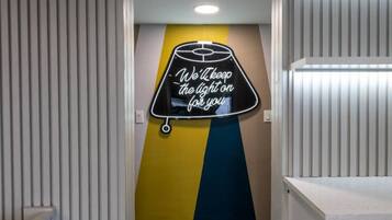 A hallway with a neon sign on the wall that reads 'We'll keep the light on for you.'