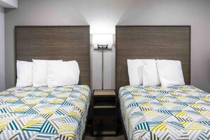 A hotel room with two beds, each with a patterned bedspread, a nightstand, and a wall-mounted light fixture between the beds.