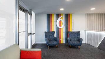 A modern waiting area with two armchairs, a red cushion, and a large number '6' on the wall.