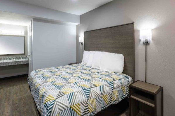 Une chambre d’hôtel avec un lit, une table de chevet, une lampe fixée au mur et une porte.