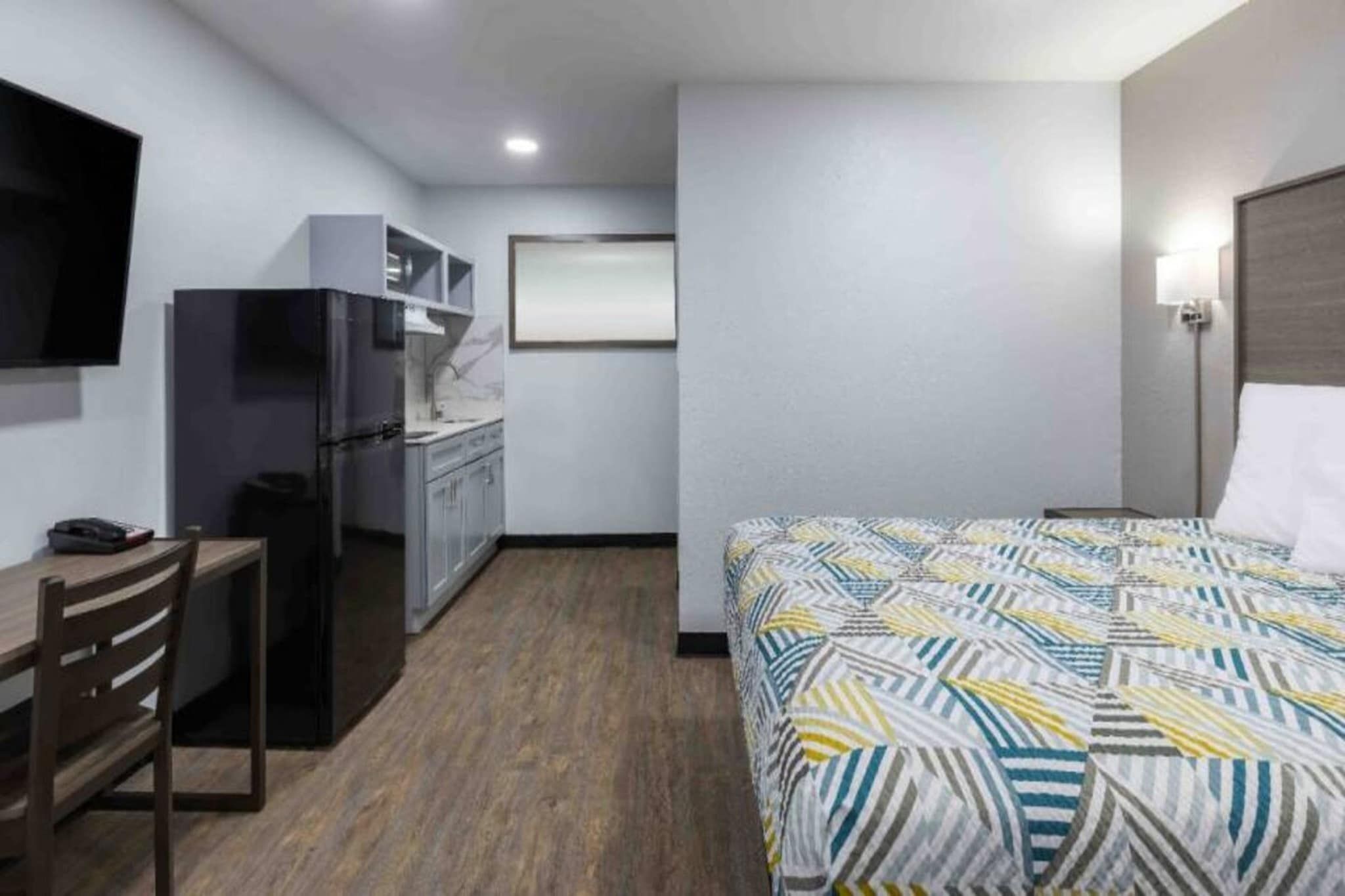 A hotel room with a bed, a desk, a chair, a refrigerator, and a television.