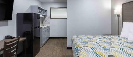A hotel room with a bed, a desk, a chair, a refrigerator, and a television.