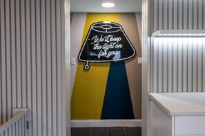 Un pasillo con un letrero de neón en la pared que dice 'Dejaremos la luz encendida por ti'.