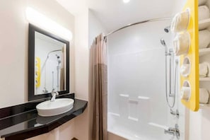 Um banheiro moderno com pia redonda, espelho, chuveiro com porta de vidro e porta-toalhas.