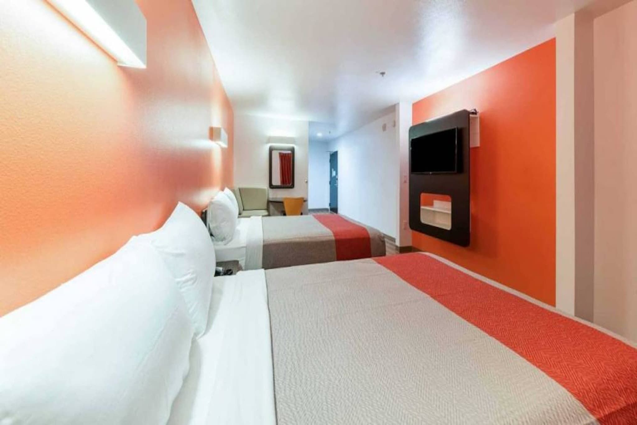 A hotel room with two beds, a TV mounted on the wall, and a red carpet.