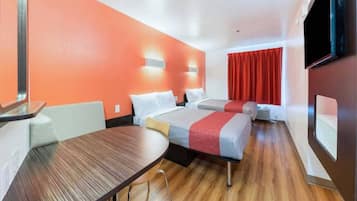 A hotel room with two beds, a wooden table, and a TV.