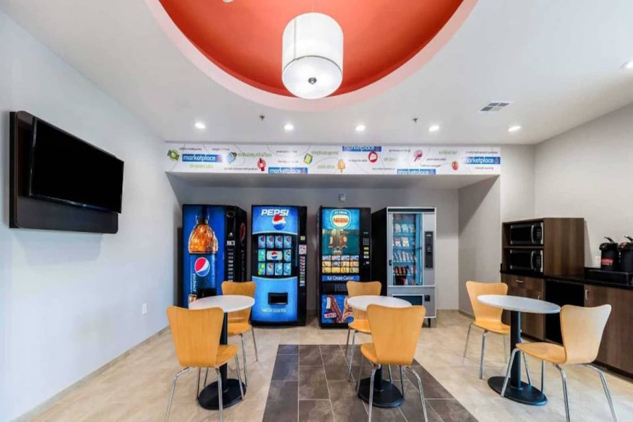 A modern interior with vending machines, seating areas, and a flat-screen TV mounted on the wall.