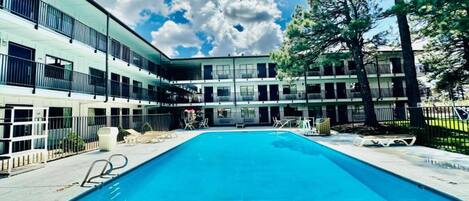 Une piscine avec des chaises longues, un bâtiment doté de nombreux balcons et un ciel dégagé.