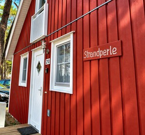 A red building with a sign reading 'Strandperle' and a door marked with the number 210. - Cozy vacation home in Baabe with a sauna, hot tub, fireplace, and south-facing terrace—sleeps up to 6 people (Baabe)
