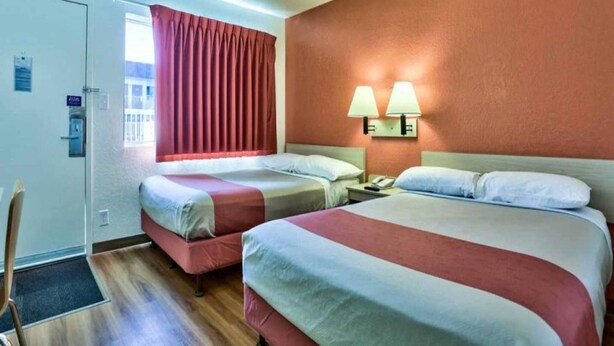 A hotel room with two beds, a window with curtains, a nightstand with a lamp, and a door with a lock. - 2 Full Beds | Micfridge, Smoking (Flaggstaff)