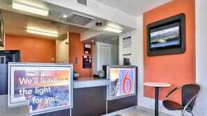Uma área de recepção de hotel com balcão, cadeira e televisão na parede.