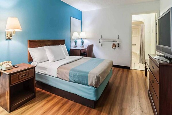 A hotel room with a bed, bedside table, lamp, and a television. - 1 King Bed | Non-Smoking (Southgate)