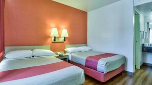 Quarto de hotel com duas camas, uma mesa de cabeceira e uma luminária fixada na parede.