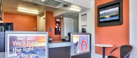 A hotel reception area with a counter, a chair, and a television mounted on the wall.