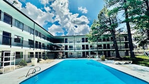 En swimmingpool med solstolar, en byggnad med flera balkonger och en klar himmel.