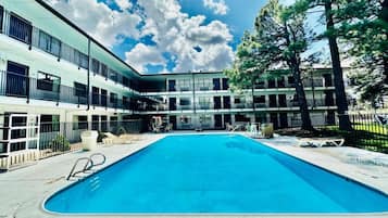En swimmingpool med liggestole, en bygning med flere balkoner og en klar himmel.