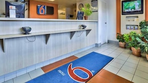 En hotellobby med en receptionsdisk, en klocka, en tv och en blå matta med en logotyp.