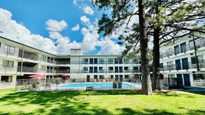 En byggnad med flera våningar, med en swimmingpool, omgiven av ett inhägnat område och träd.