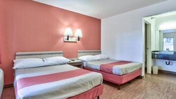 Et hotelværelse med to senge, et natbord, en lampe ophængt på væggen og et badevrelse, der kan ses gennem en åben dør.