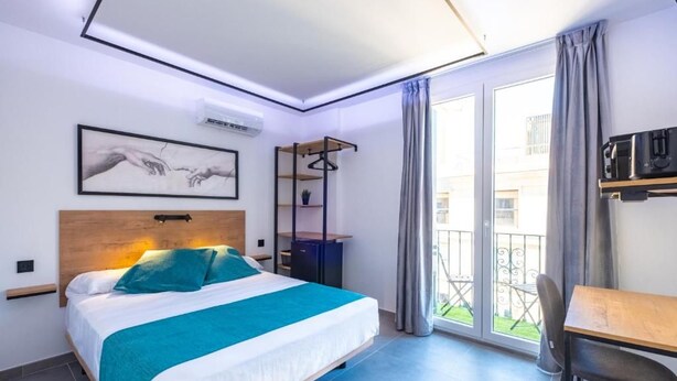 Quarto de hotel com cama, escrivaninha, cadeira, varanda com vista e um quadro na parede.